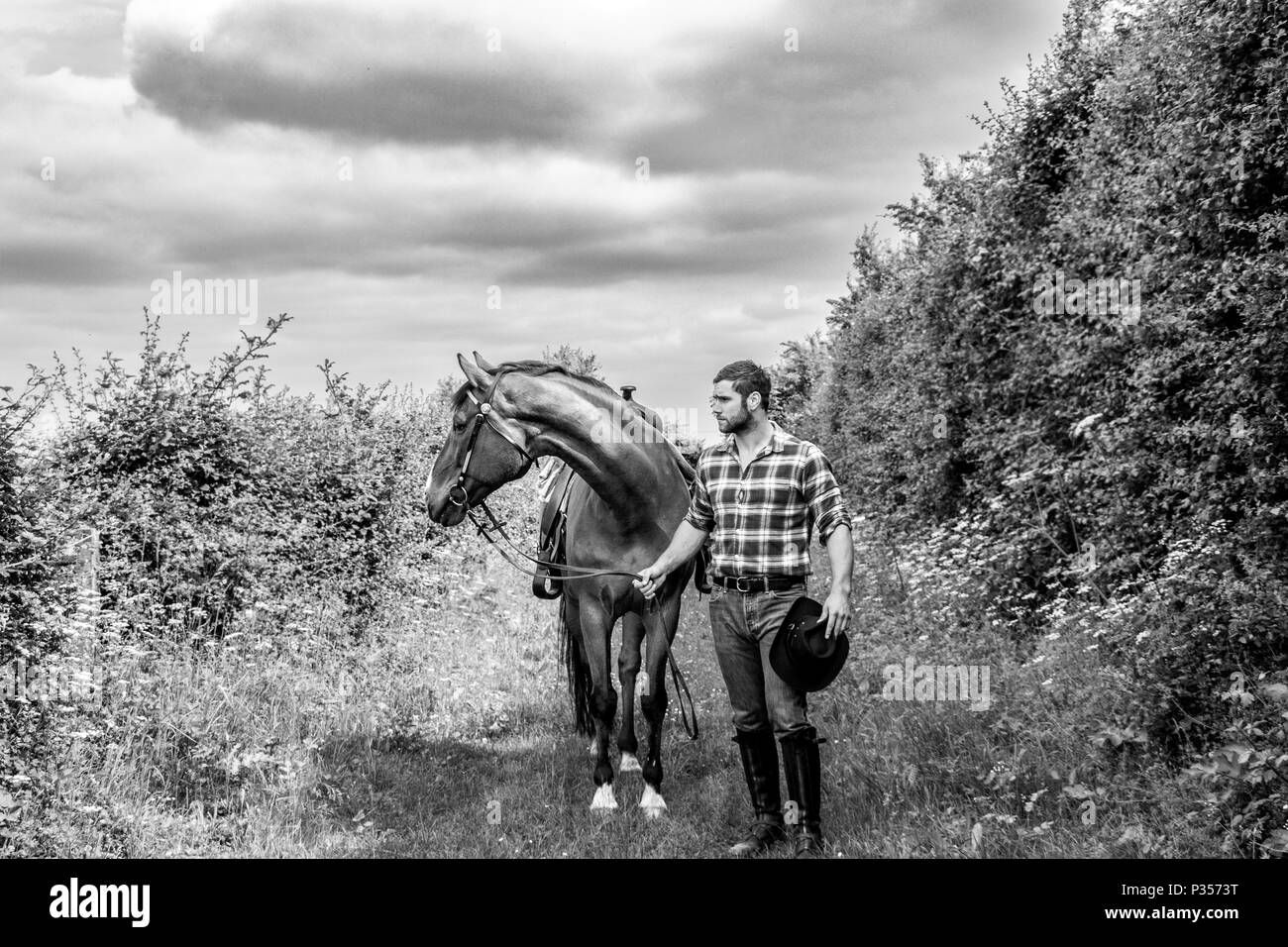 Good looking, hunky cowboy rides horse with boots, chequered shirt and