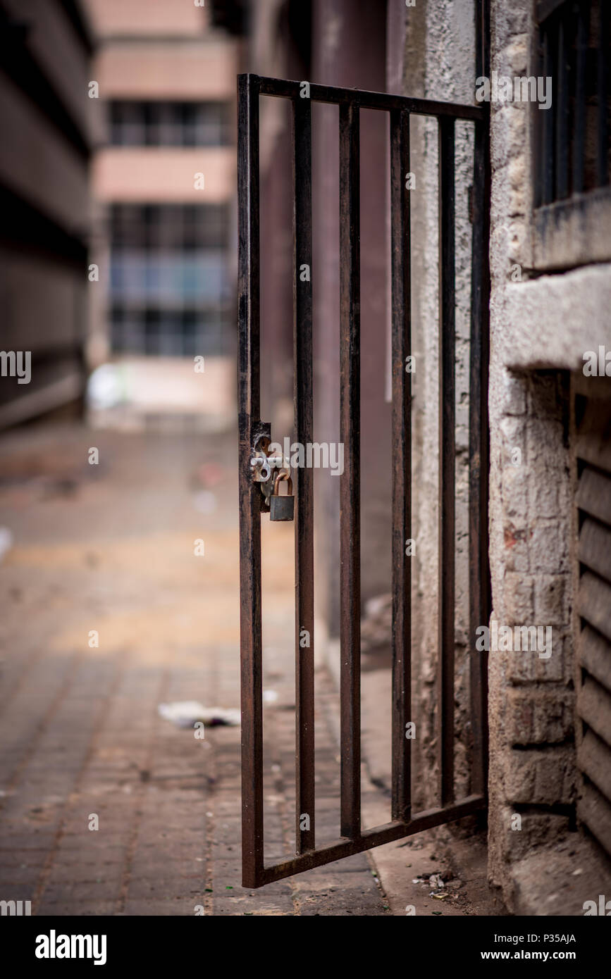 A metal doorway with padlock stands open in a dirty alleyway. Johannesburg inner city Stock Photo