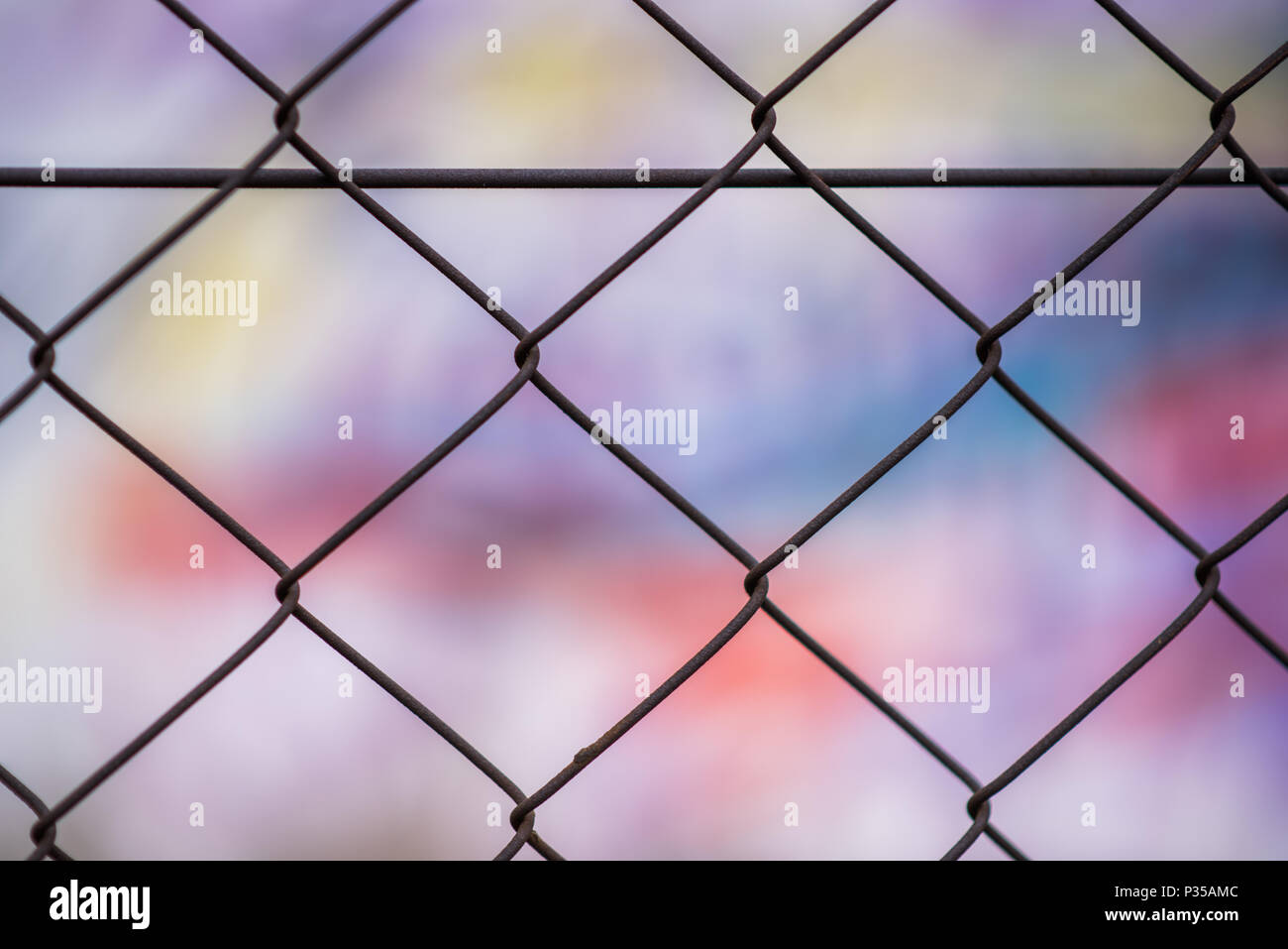 An abstract patterend shot of wire mesh fencing with blurred colorful graffiti in the background in Johannesburg inner city Stock Photo
