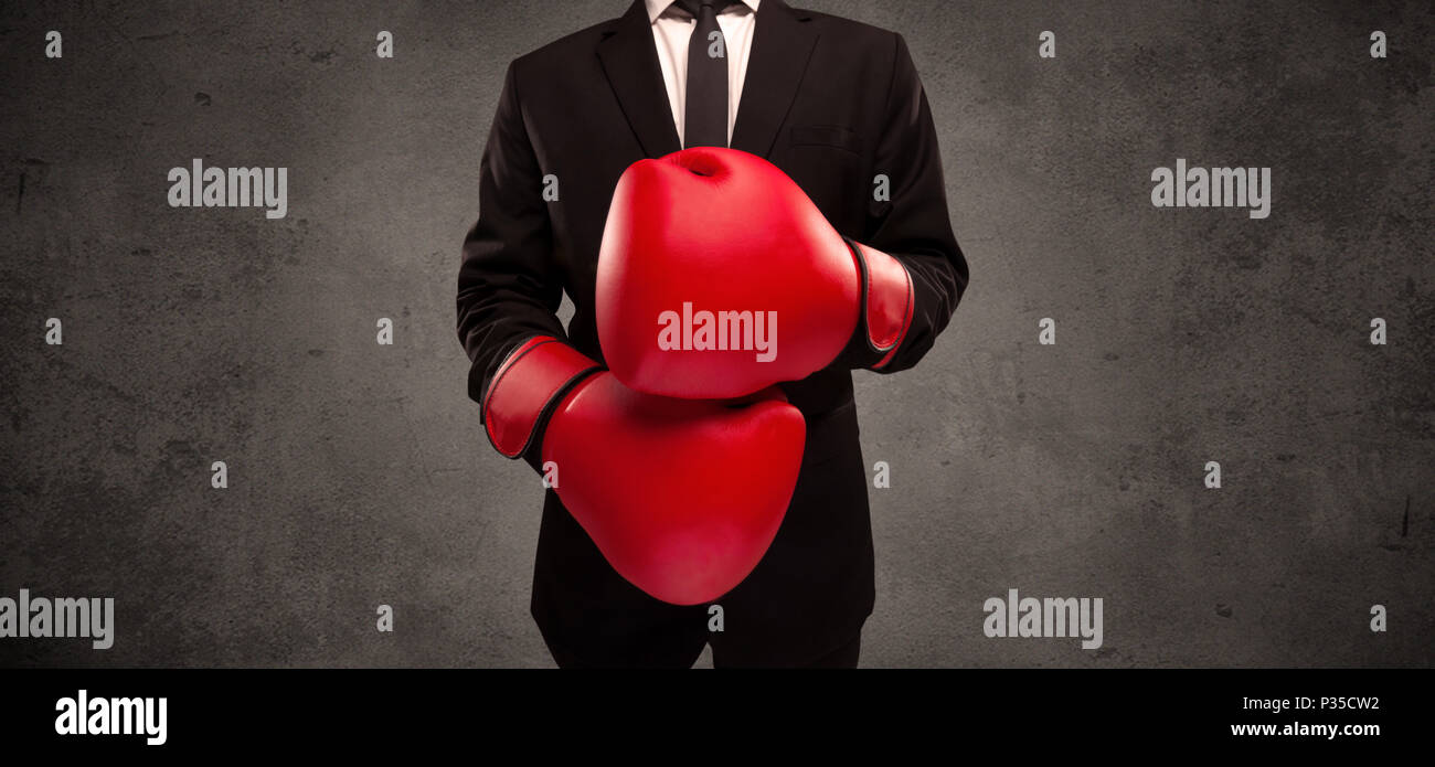 A well dressed sales person standing with red boxing gloves on his hand in front of urban grey wall background concept. Stock Photo