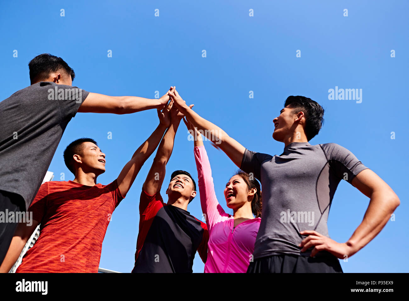 team of asian young adult sportsmen and sportswoman putting hands together to show unity and teamwork spirit. Stock Photo