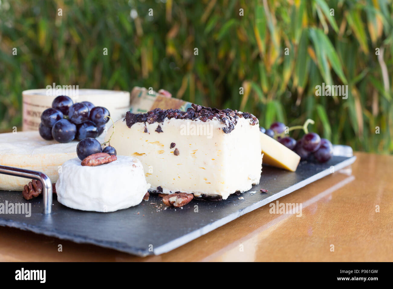 A platter with various cheeses like Gruyère, goat cheese decorated with grapes and nuts. These foods are eaten for dessert or after a hearty meal. Stock Photo
