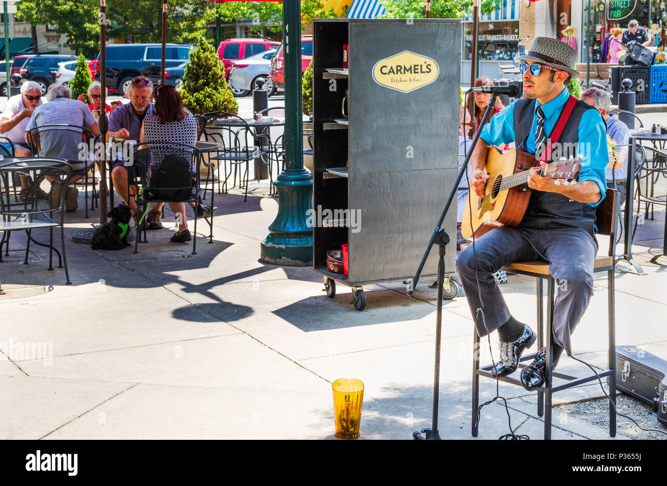 ASHEVILLE, NC, USA-10 JUNE 18:  A street performer sings and plays guitar, while patrons dine outside at Carmel's Kitchen and Bar. Stock Photo