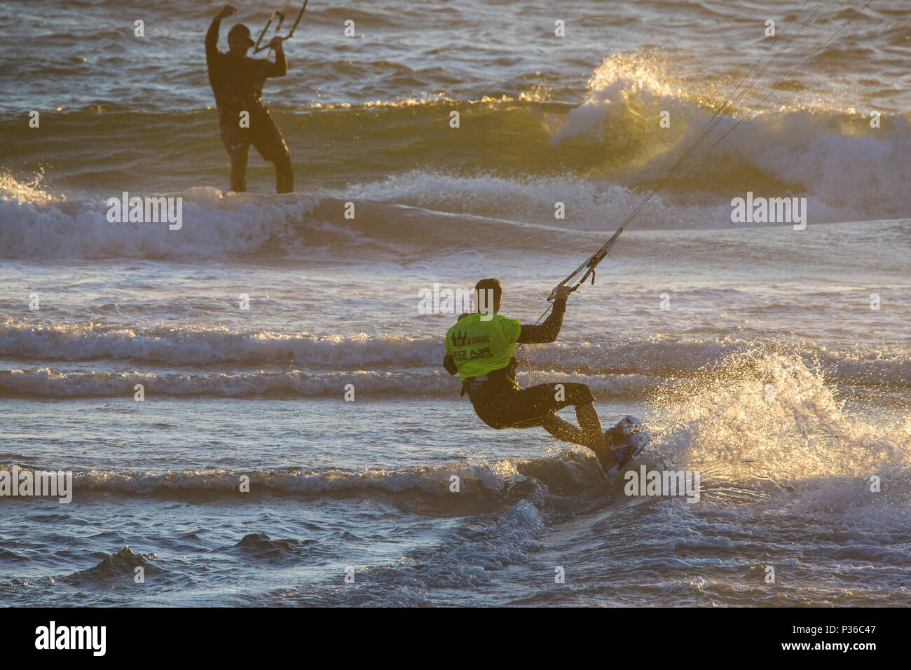 two male competitors kiteboarding or kitesurfing riding the waves at sunset at Kite Beach