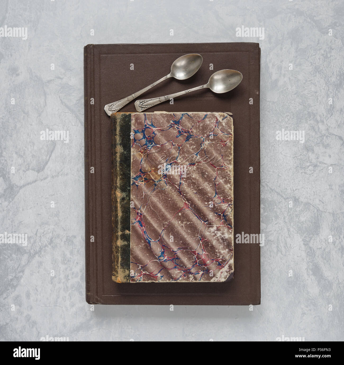 Two teaspoons lying on an old recipes books on a marble background Stock Photo