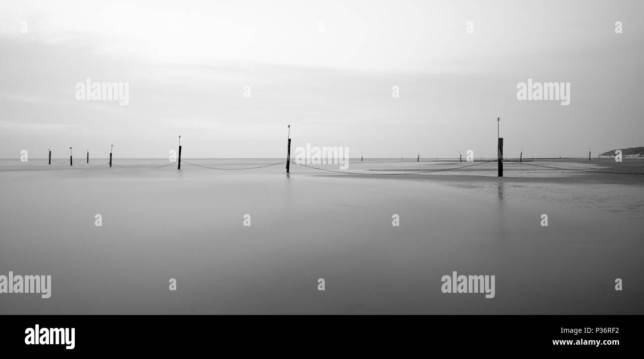 A row of poles marking the swimming area leading into the North Sea in Norderney, Germany. Long exposure shot during upcoming high tide. Stock Photo