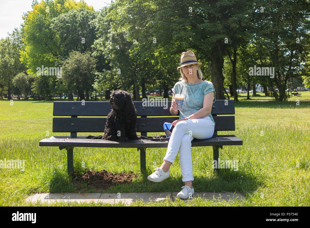 A woman shares her croissant with her pet dog on a park bench whilst ...