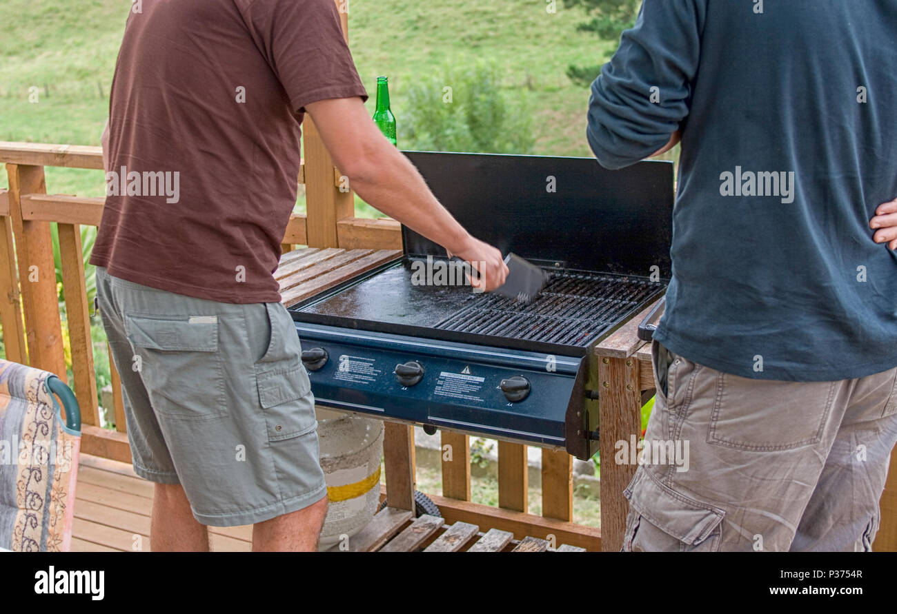 Two men at barbecue while cleaning the grate Stock Photo Alamy