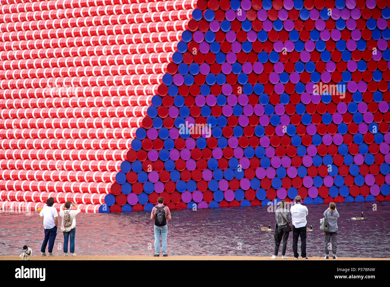 People looking at Christo's first UK outdoor work, The Mastaba, a 20m high installation made up of 7,506 horizontally stacked barrels and which will be 20m high, 30m wide and 40m long, to be displayed on Serpentine Lake until 23 September 2018. Stock Photo