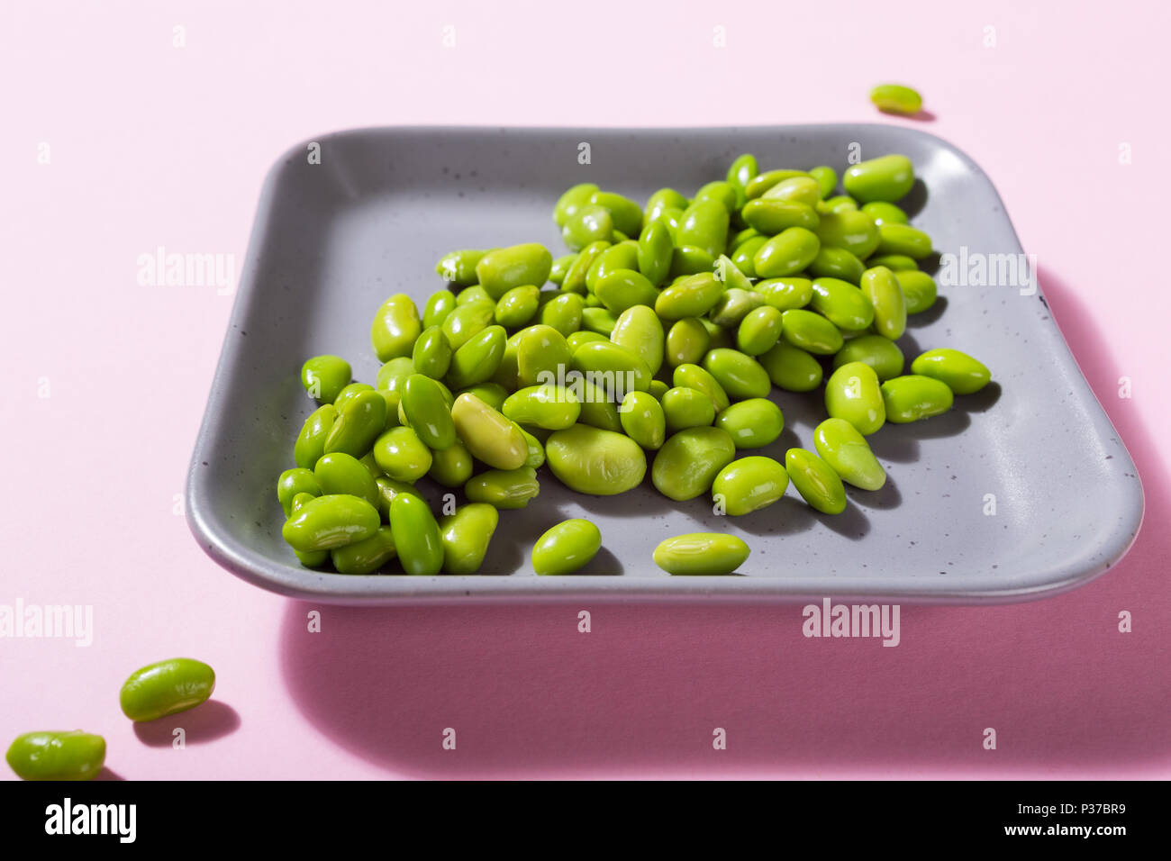 Green fresh soybeans on gray square plate on pink background. Healthy food concept with coppy space. Stock Photo