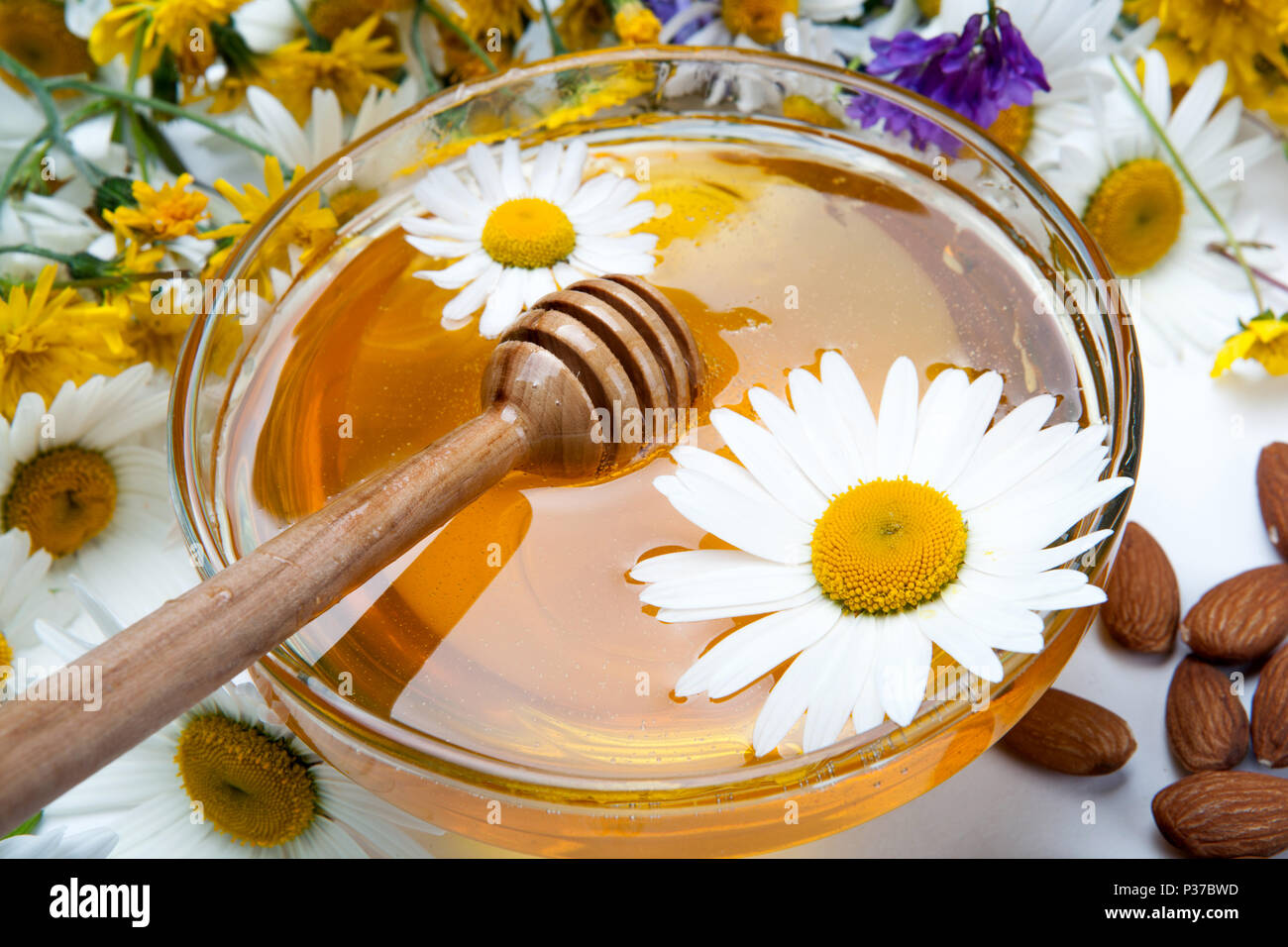fresh honey in a bowl and honey stick and flowers Stock Photo