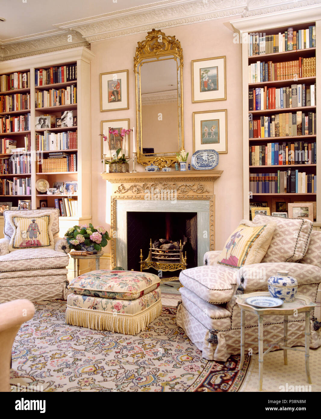 Fitted bookcases on either side of fireplace in townhouse living room with ottoman and comfortable armchairs Stock Photo