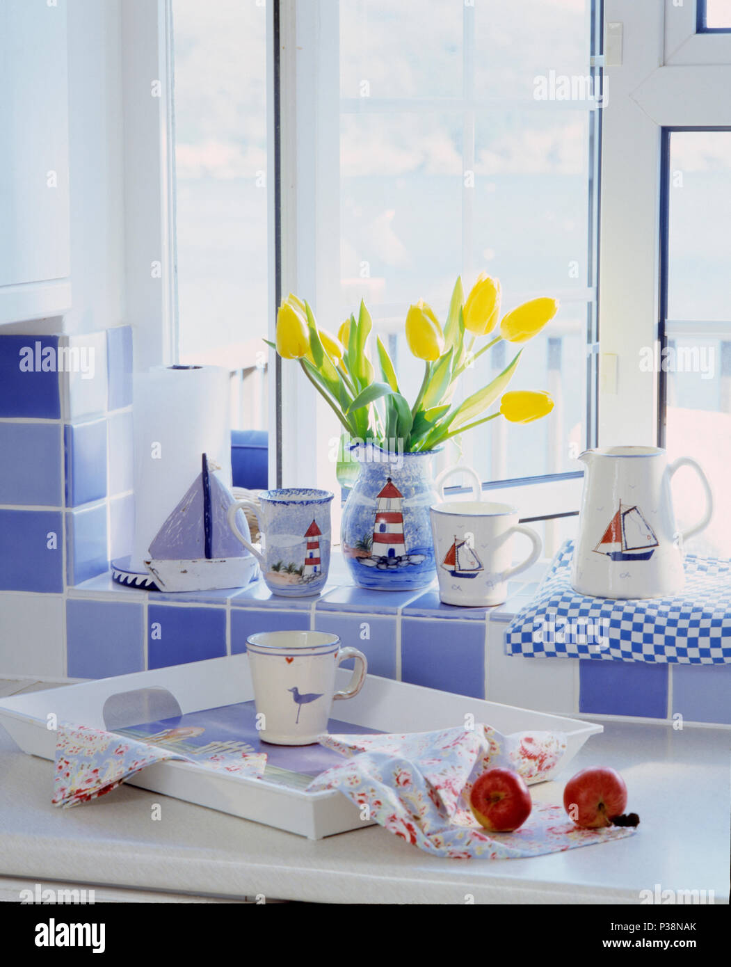 Close-up of collection of coastal crockery on blue+white tiled windowsill above white tray on kitchen worktop Stock Photo