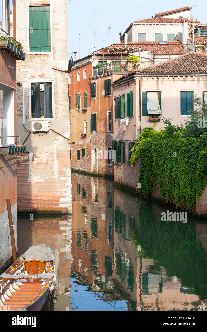 Scenic reflections at sunset on a canal in Cannaregio, Venice,  Veneto, Italy with a wooden boat and ancient houses Stock Photo