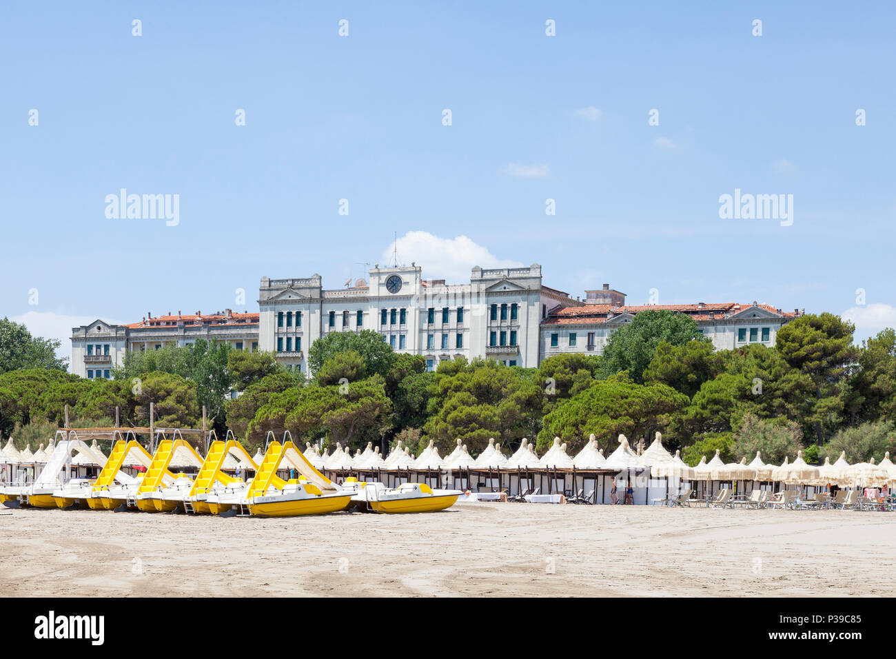 Colourful yellow recreational boats for hire and cabanas on a private beach on Lido di Venezia, Venice, Veneto, Italy with the ex Grand Hotel les Bain Stock Photo