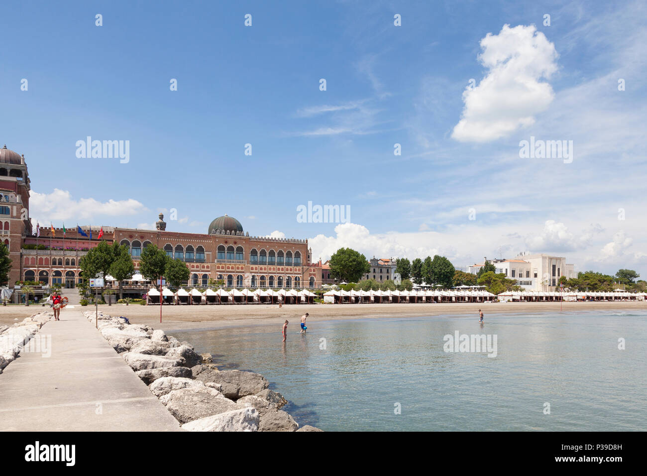 View from the breakwater of the seashore, beach,  Hotel Excelsior and Casino, Lido di Venezia, Venice, Veneto, Italy with people bathing and cabanas Stock Photo