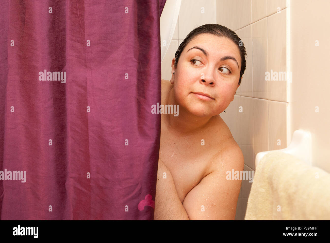 Woman peeks out behind shower curtain curiously Stock Photo