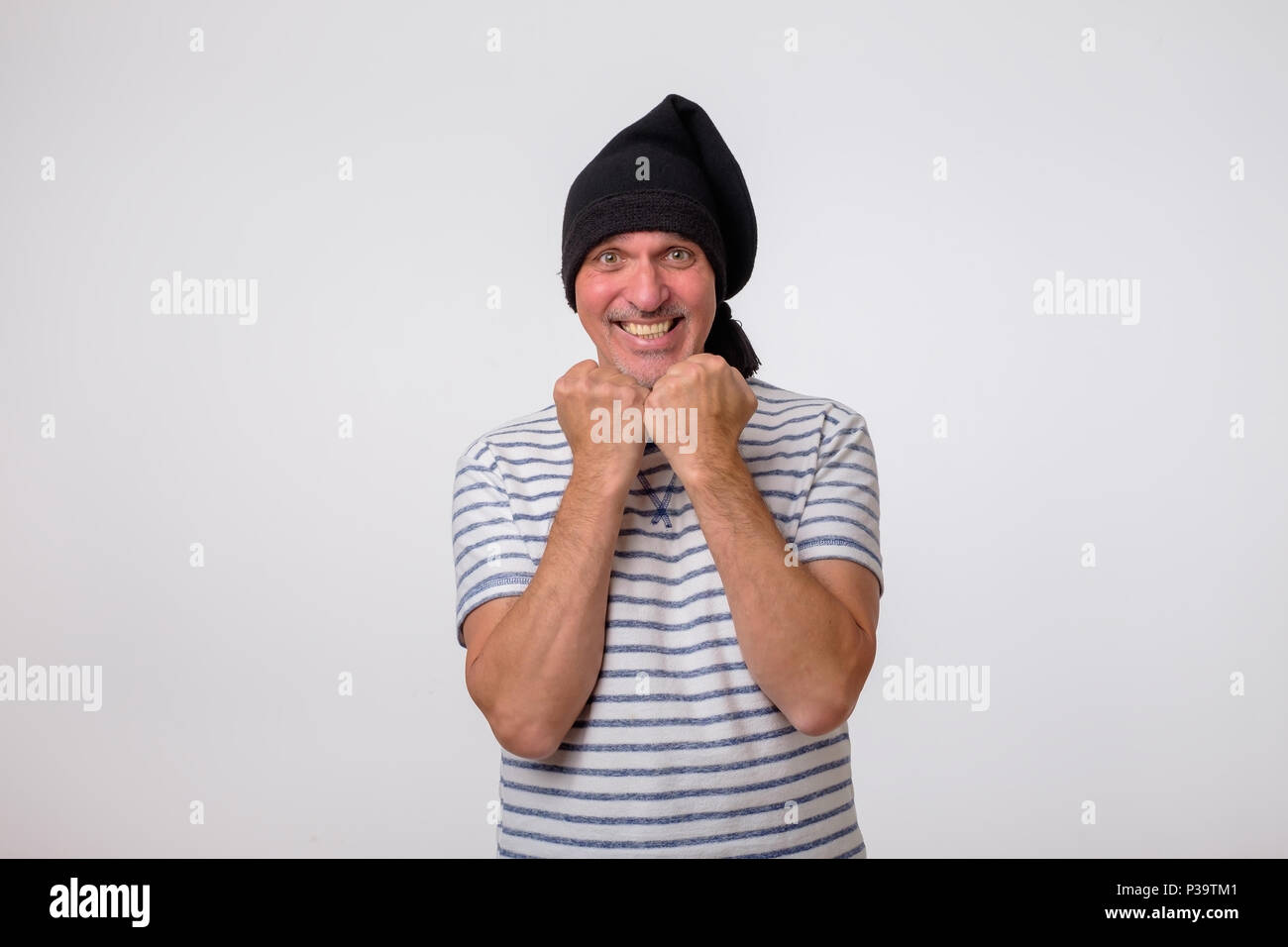 Mature man in black cap celebrating victory over gray background. Concept of happy triumph Stock Photo