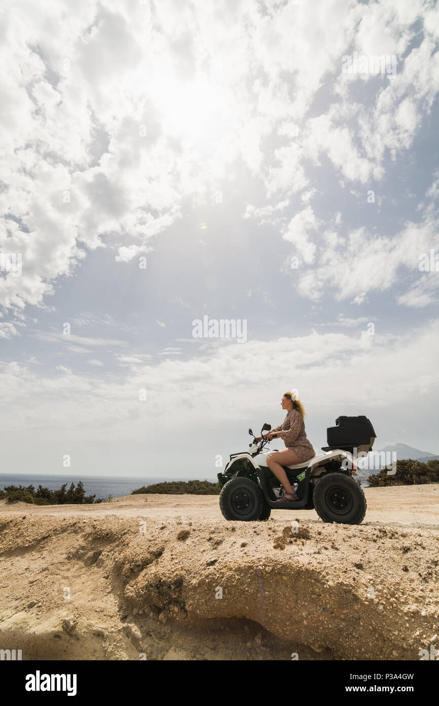 Young woman driving rental quad bike on seaside road in Milos island