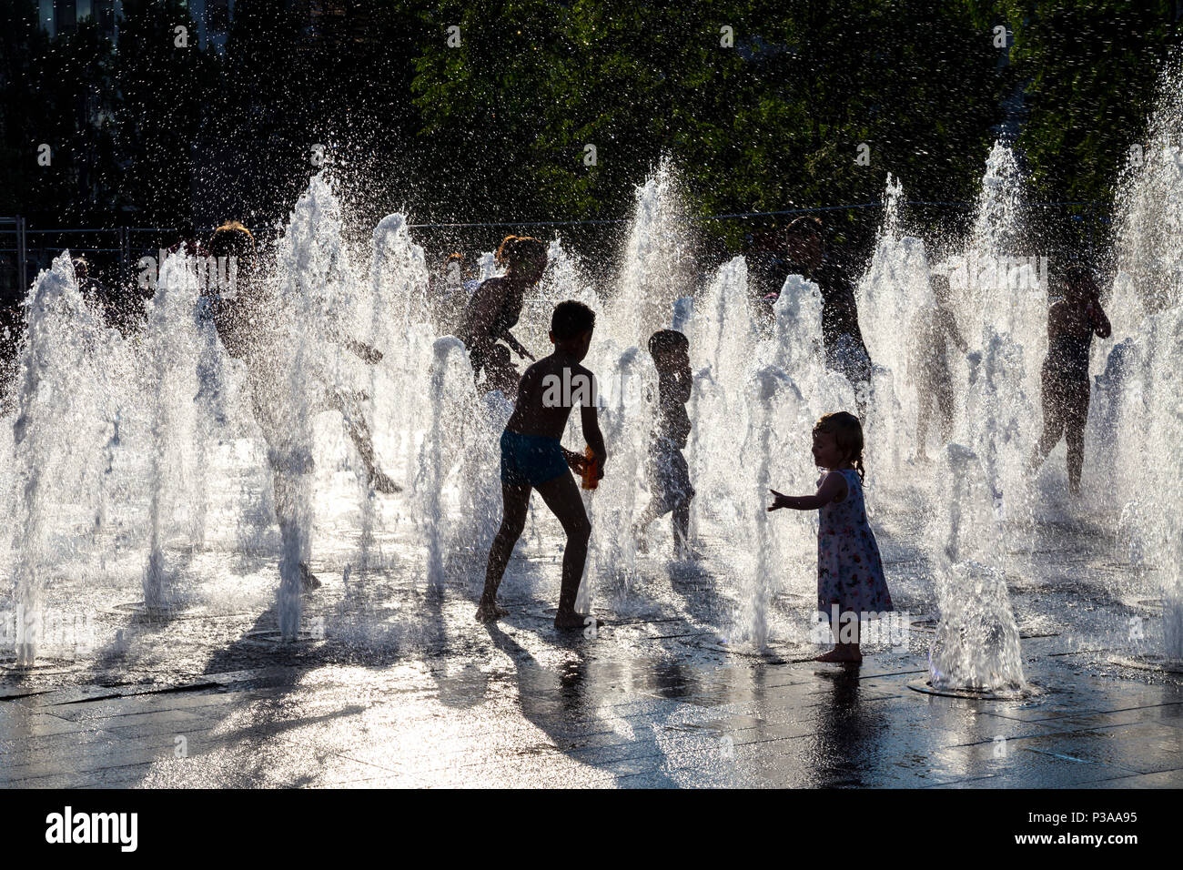 Silhouettes of children running though a fountain in the summer, Piccadilly Gardens, Manchester, UK Stock Photo