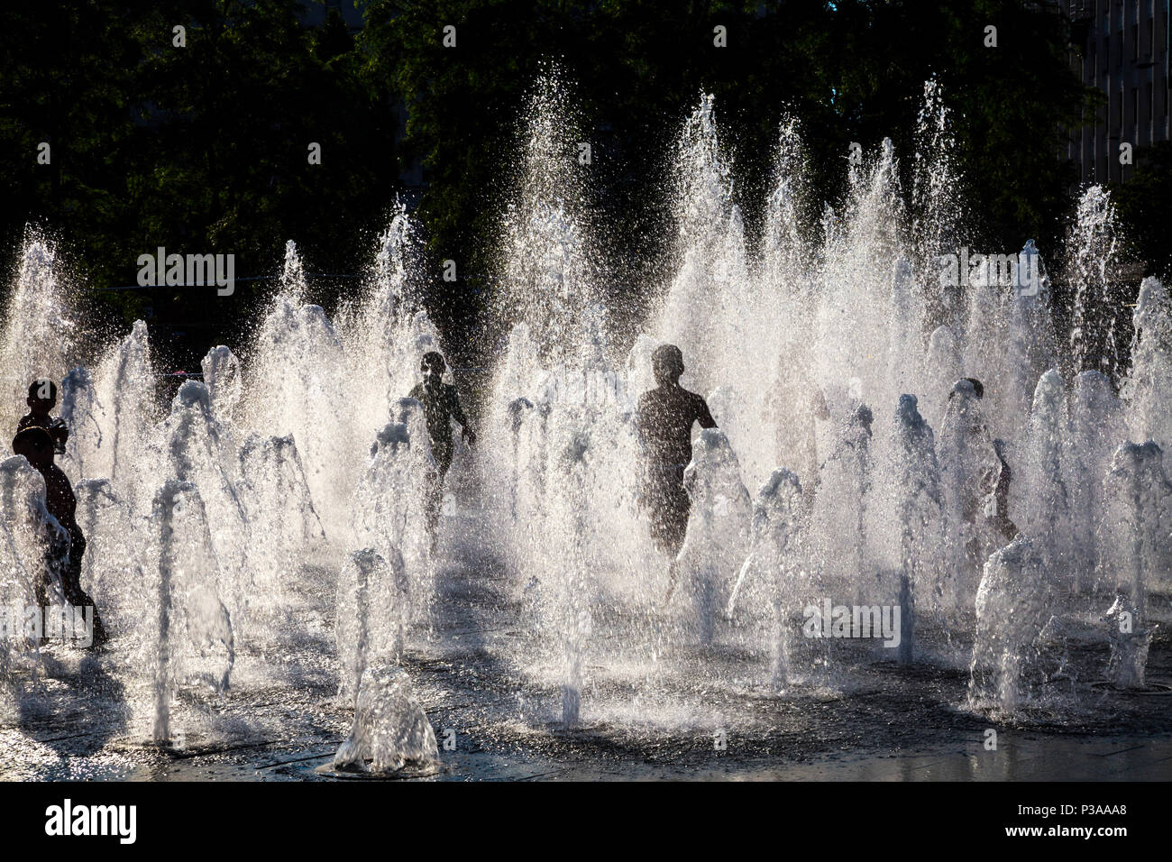 Silhouettes of children running though a fountain in the summer, Piccadilly Gardens, Manchester, UK Stock Photo