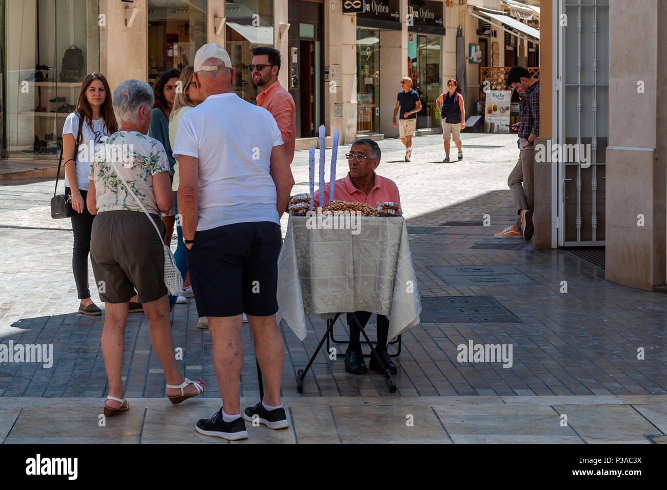 Tourists/customers stop at a stall selling peanuts and talk to the peanut vendor in Malaga, Spain. Stock Photo