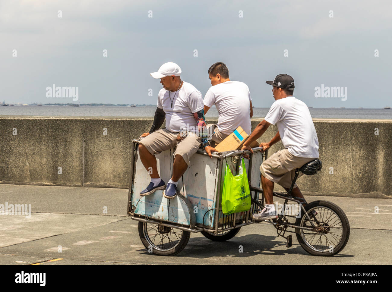 3 men on tricycle cart on Manila coast in the Philippines Stock Photo