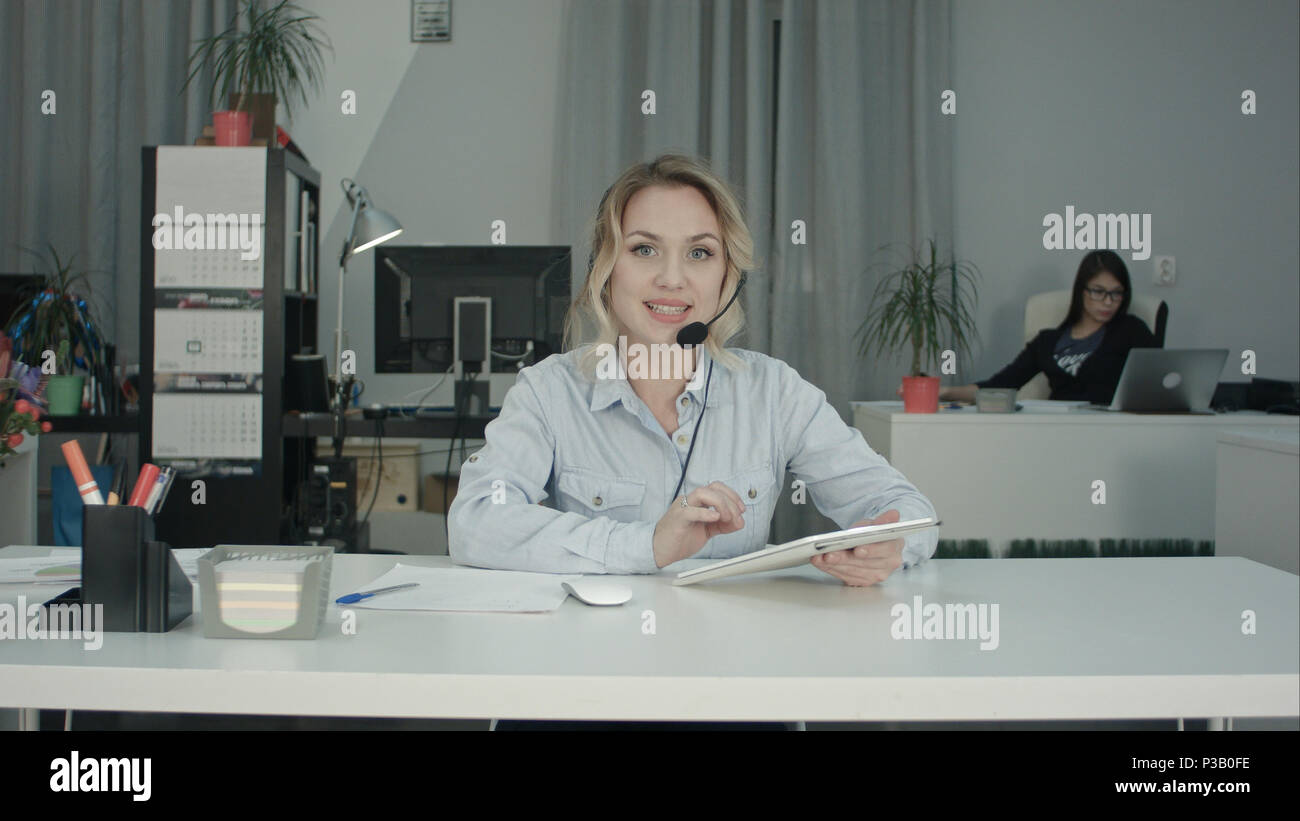 Smiling call center agent using tablet and talking to the camera Stock Photo