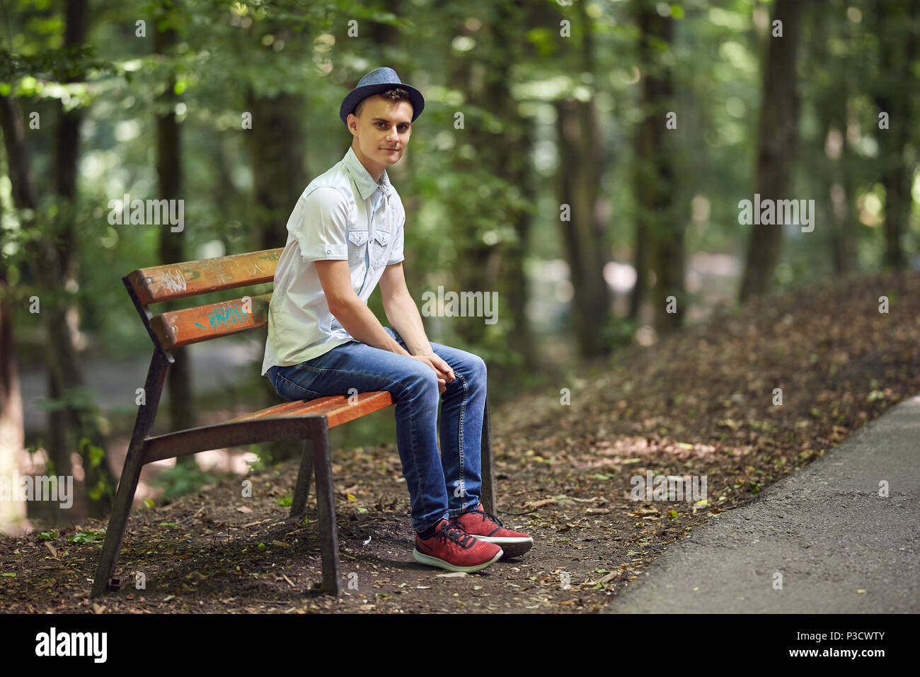 Happy handsome young man sitting on a bench in the park Stock Photo - Alamy