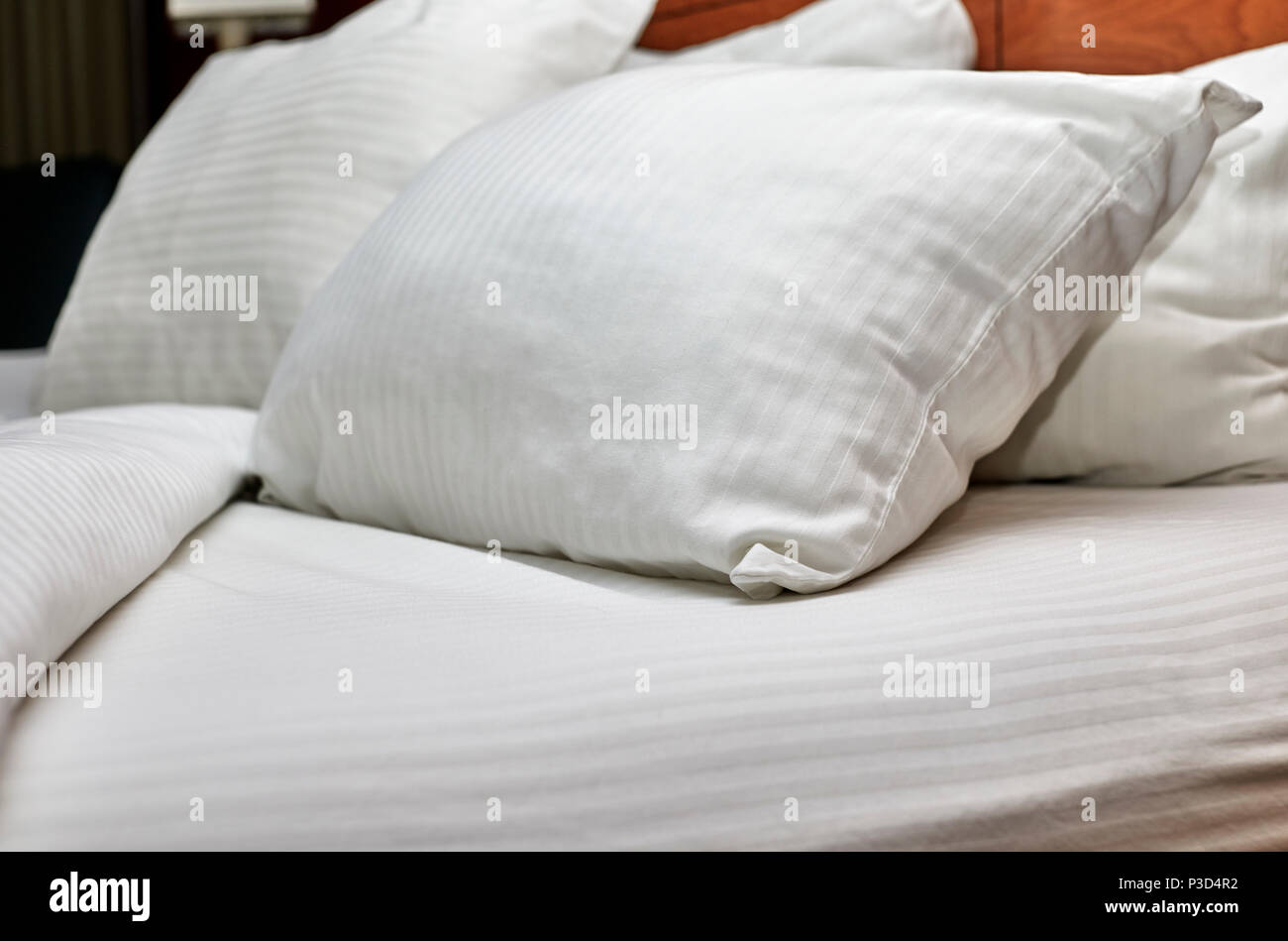 White down pillows leaning against a headboard with white sheets pulled down on a bed Stock