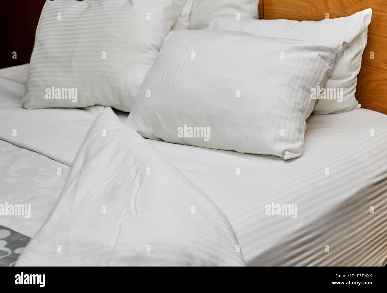 White down pillows leaning against a headboard with white sheets pulled down on a bed Stock