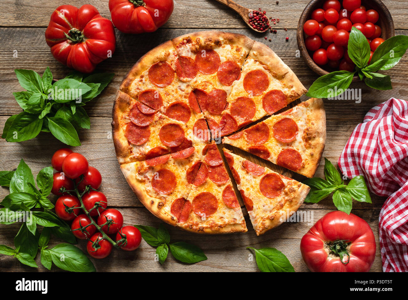 Pepperoni pizza, tomatoes and basil. Tasty pepperoni pizza on rustic wooden background. Overhead view of italian pizza Stock Photo