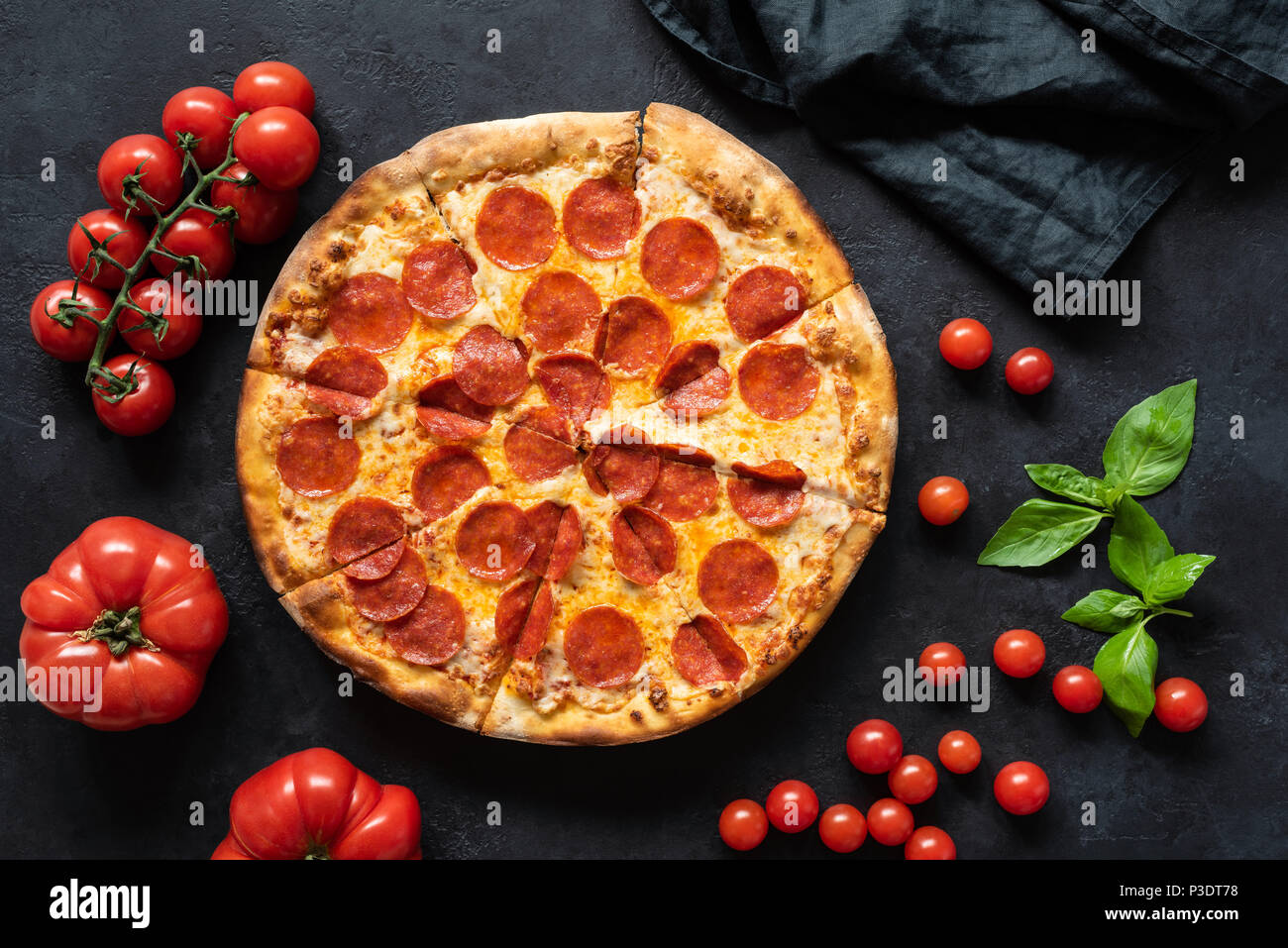 Hot pepperoni pizza on black stone background. Sliced tasty pizza with salami, cheese and tomatoes on dark table, top view Stock Photo