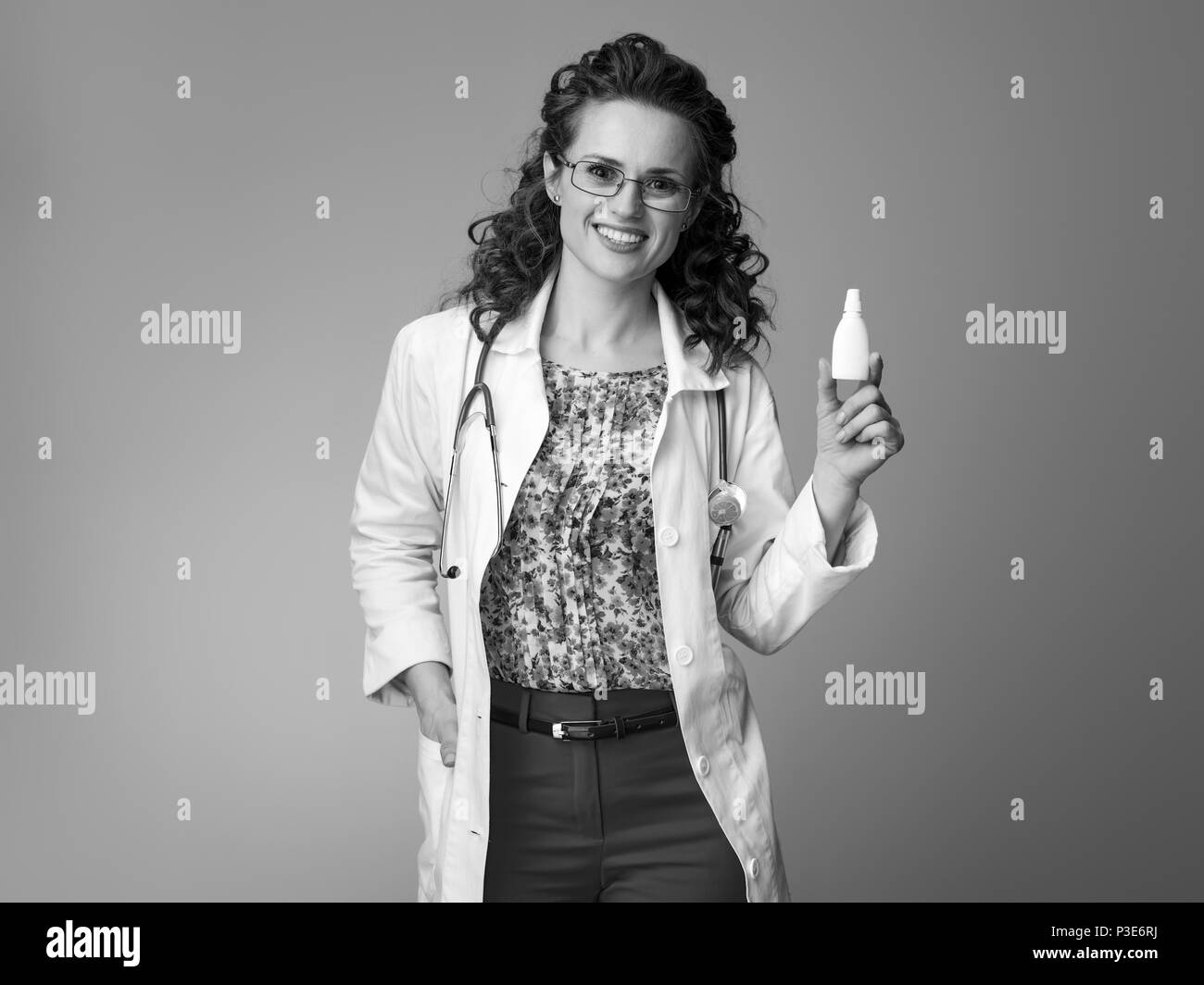 smiling pediatrist woman in white medical robe showing nasal drops isolated on background Stock Photo