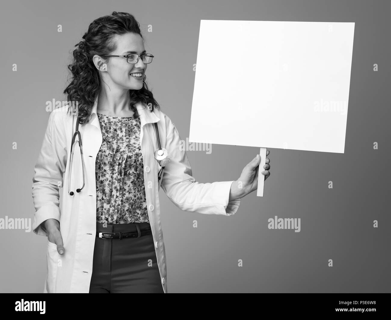 smiling paediatrician woman in white medical robe looking at placard against background Stock Photo