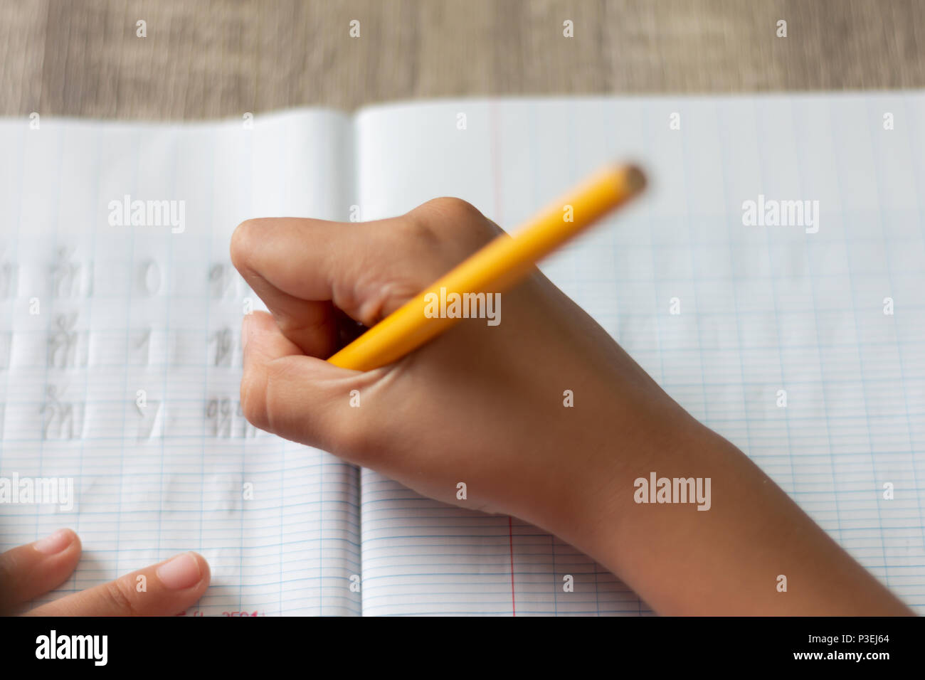 A little girl doing homework. Hand is holding a yellow pencil and writing in a notebook with high angle. Select focus shallow depth of field and blurr Stock Photo