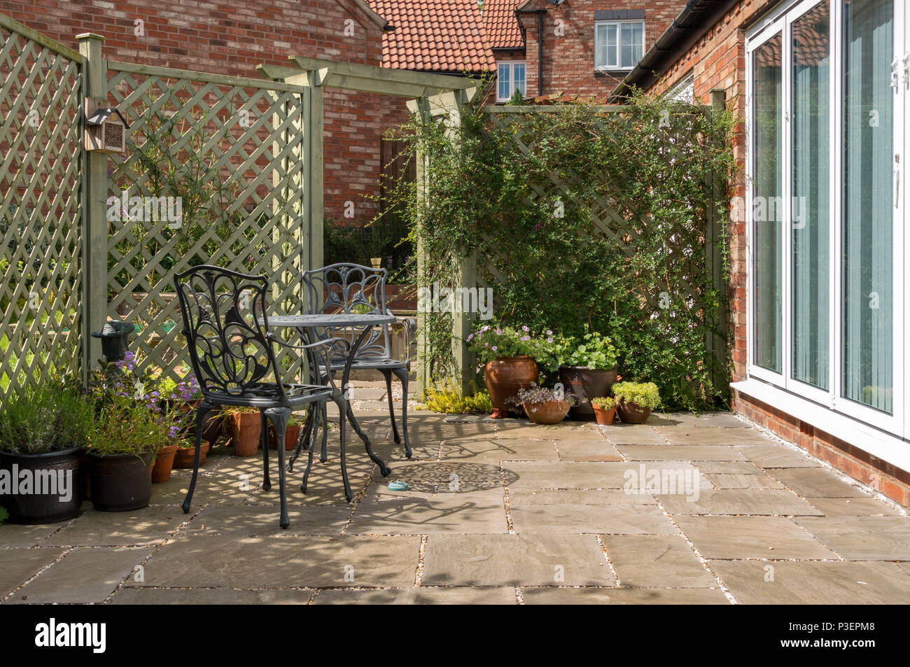 Small domestic garden patio with metal table and chairs, natural stone slabs and painted trellis Stock Photo