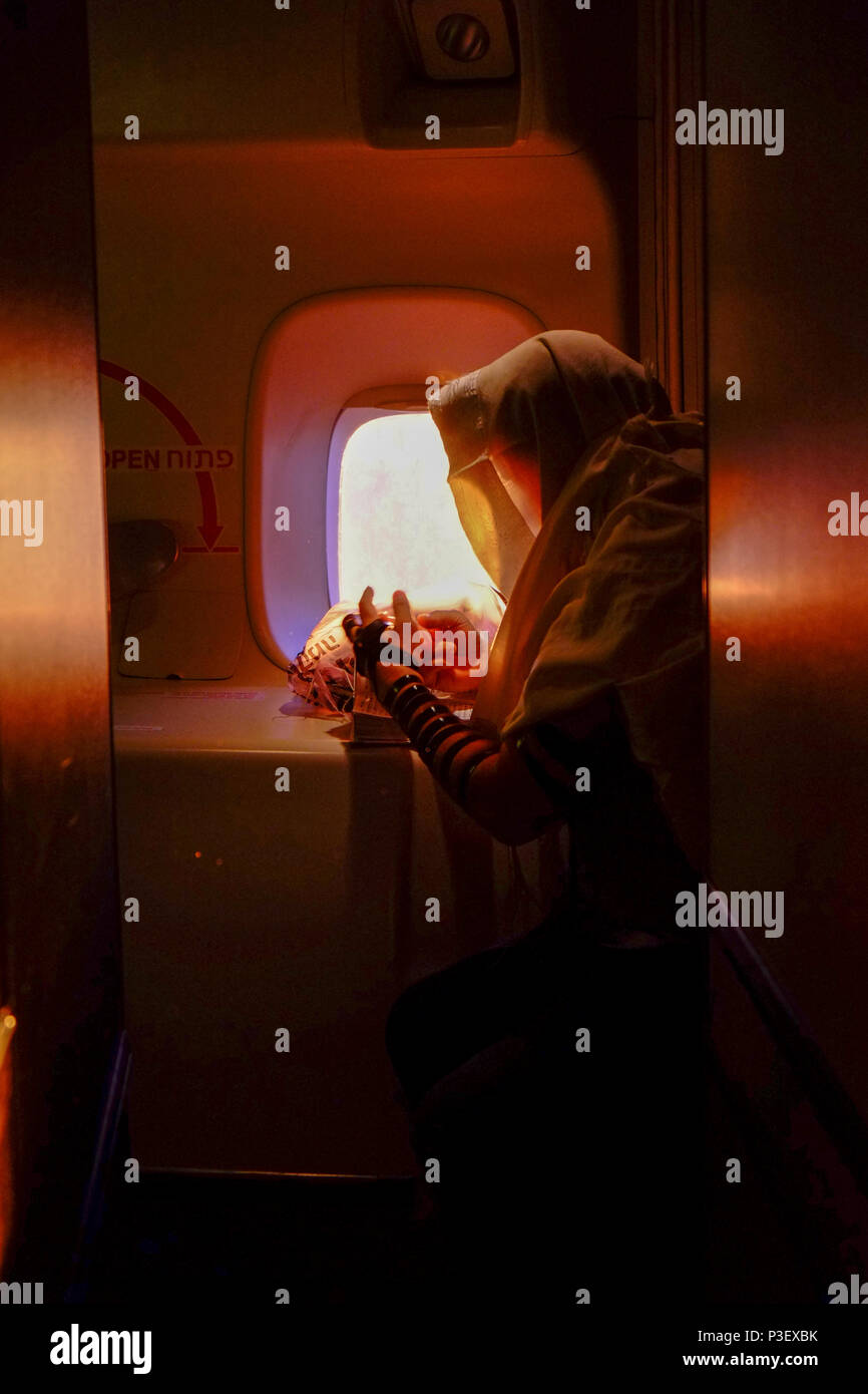 A man is putting on a tefillin and praying at sunrise inside of an airplane over the ocean Stock Photo