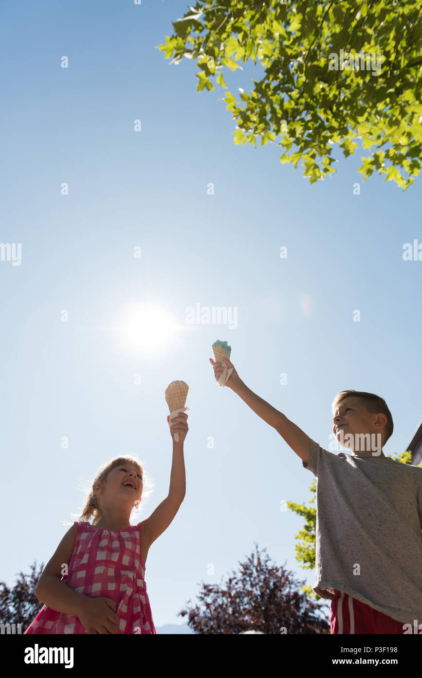 Siblings holding ice cream against sky Stock Photo
