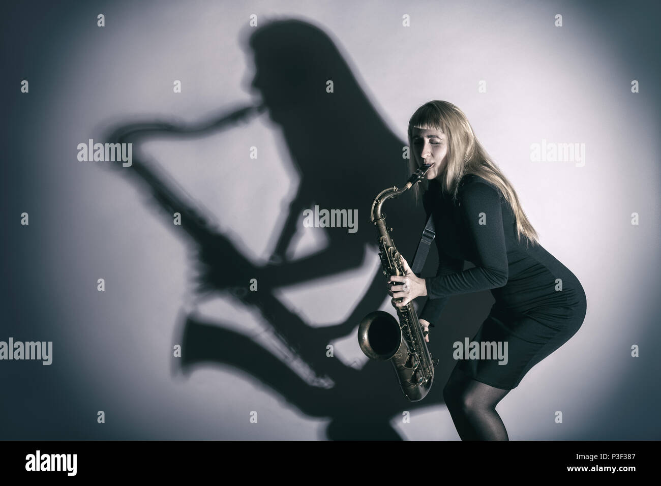 Saxophone player. Woman with a saxophone and a silhouette falling on a wall Stock Photo