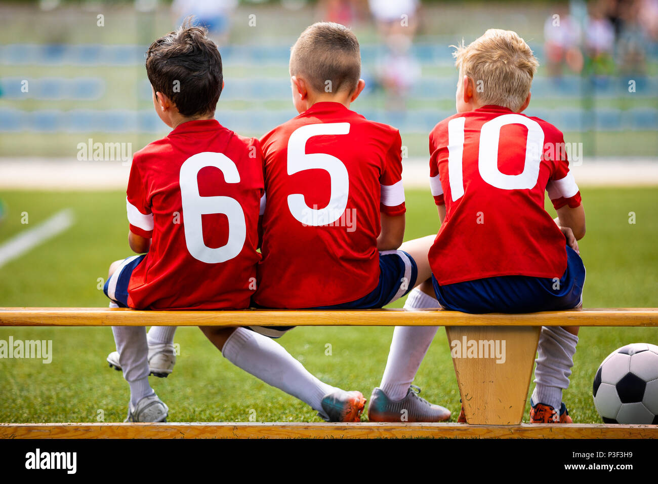 Football soccer children team. Kids substitute players sitting on a bench. Football sports tournament for young boys. Three kids watching football gam Stock Photo