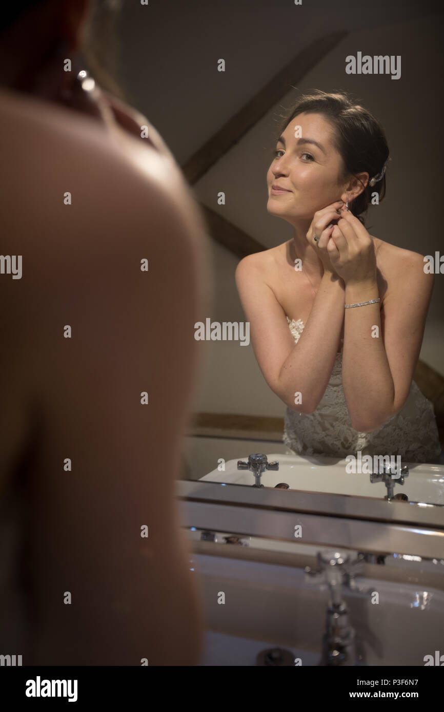 Smiling bride wearing earrings in front of the mirror Stock Photo