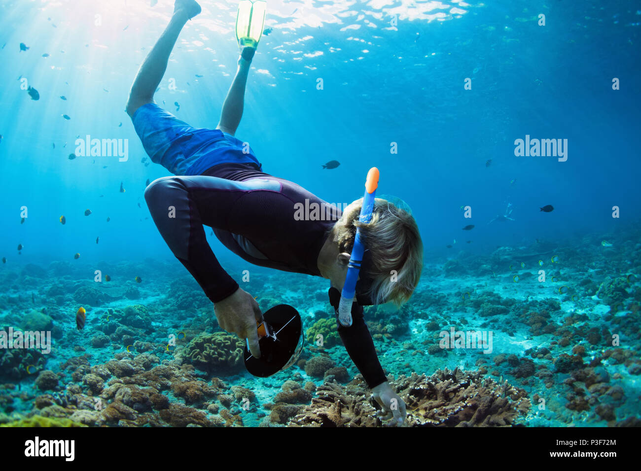 Happy family vacation. Man in snorkeling mask with camera dive underwater with tropical fishes in coral reef sea pool. Travel lifestyle, water sport o Stock Photo