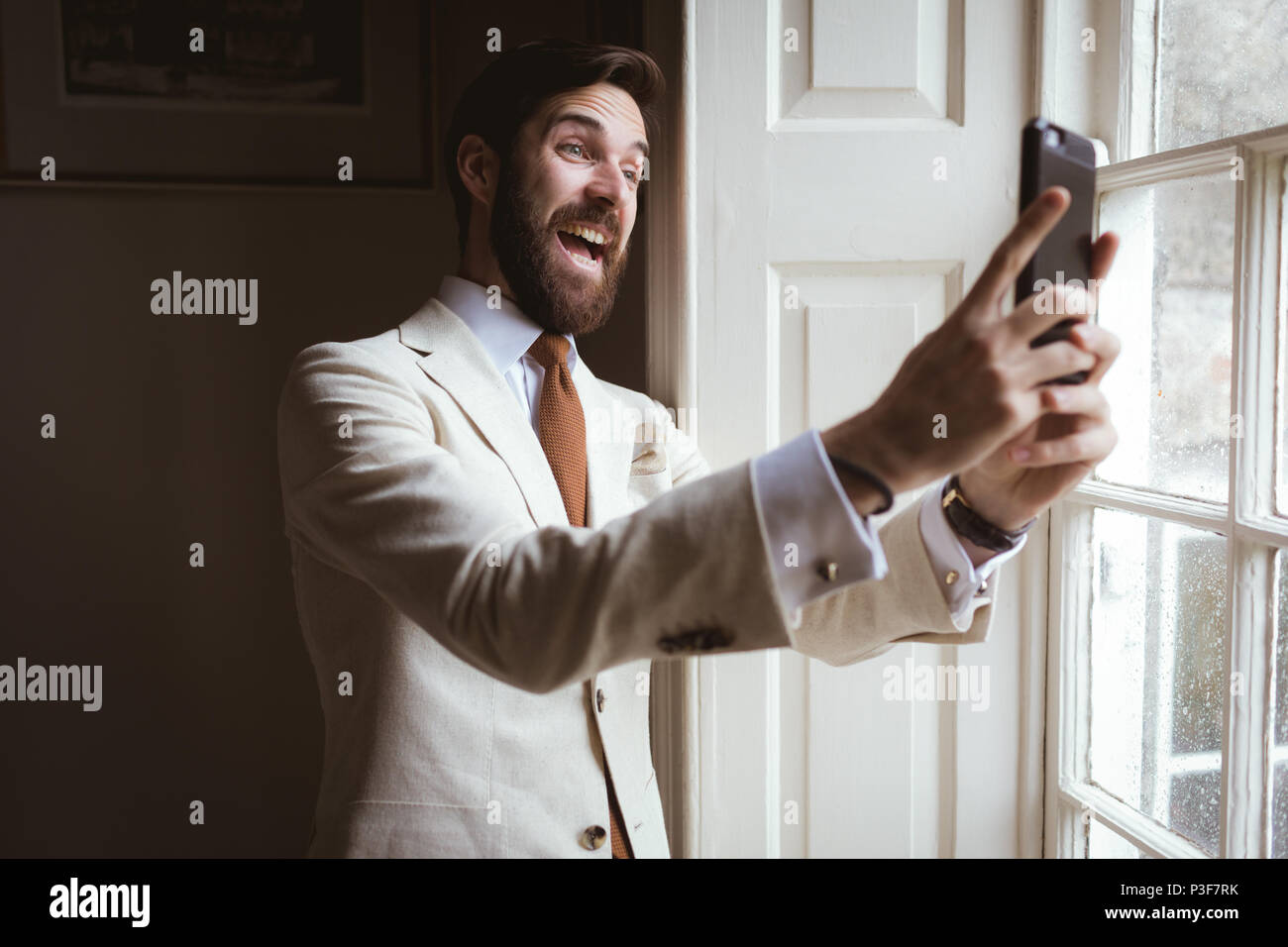 Excited groom taking a selfie near the window Stock Photo