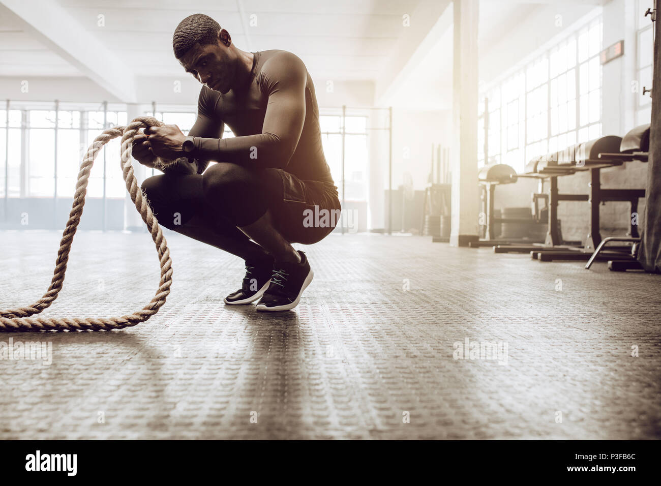 Man sitting on his toes holding a pair of battle ropes for workout. Crossfit  guy at the gym working out with fitness rope Stock Photo - Alamy