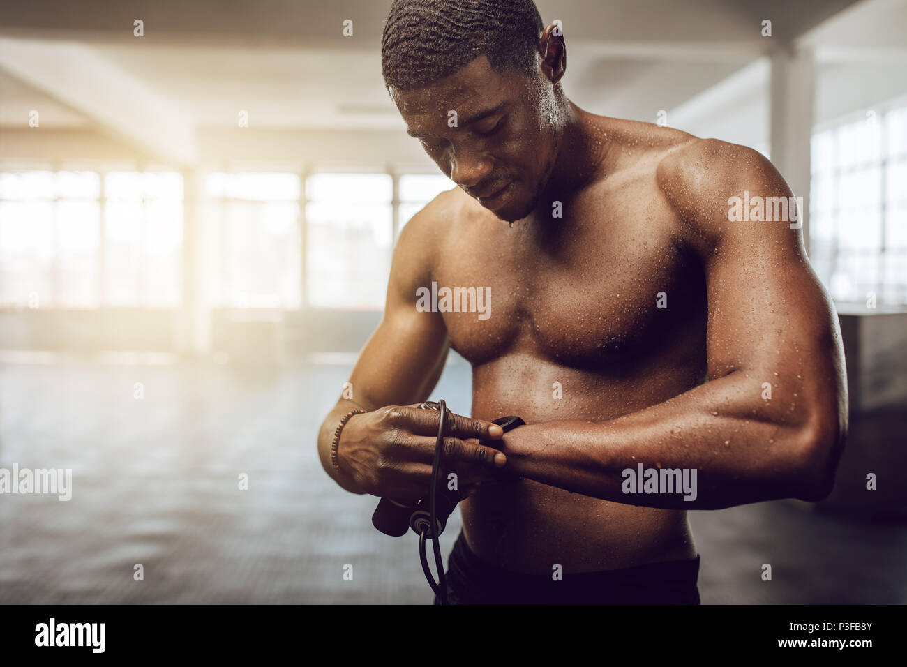 Man setting a timer in his wrist watch standing in the gym. Bare chested muscle athlete holding skipping rope with sweat all over his body after worko Stock Photo Alamy