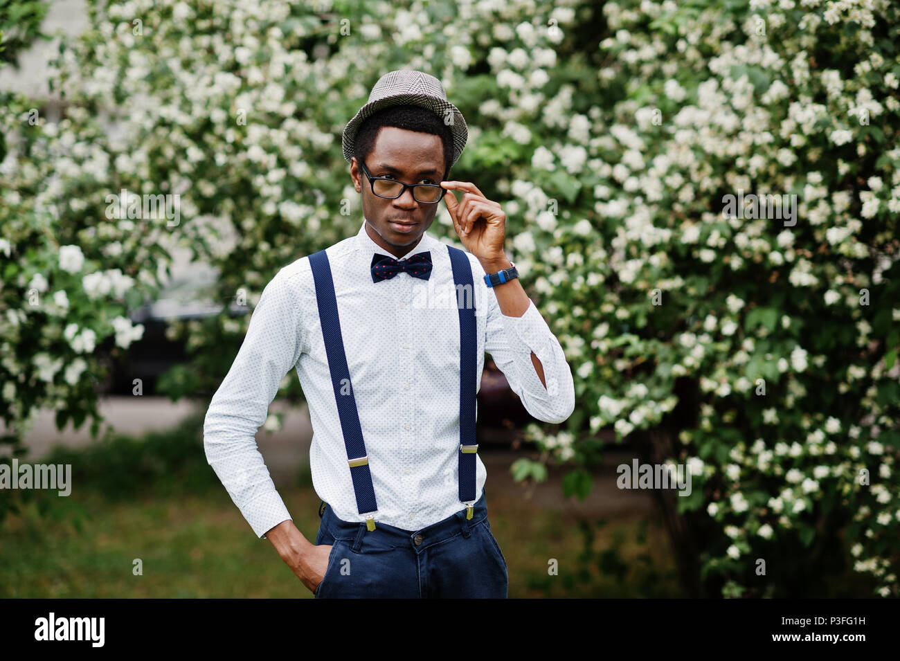 Stylish african american business man at pants with suspender and shirt with bow tie, hat and glasses posed outdoor. Stock Photo