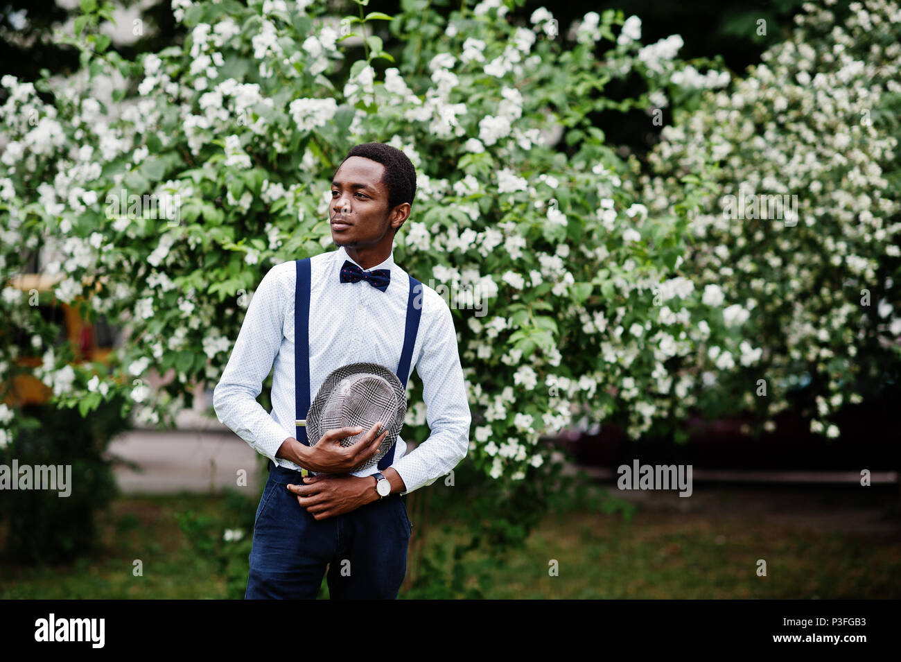 Stylish african american business man at pants with suspender and shirt with bow tie, hat posed outdoor. Stock Photo