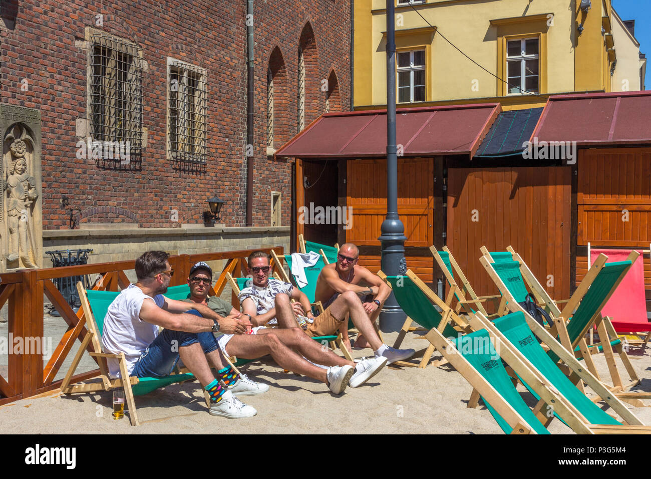 Locals and tourists relax on deckchairs in the sun on makeshift beach in the Market Square, Wrocław, Poland Stock Photo