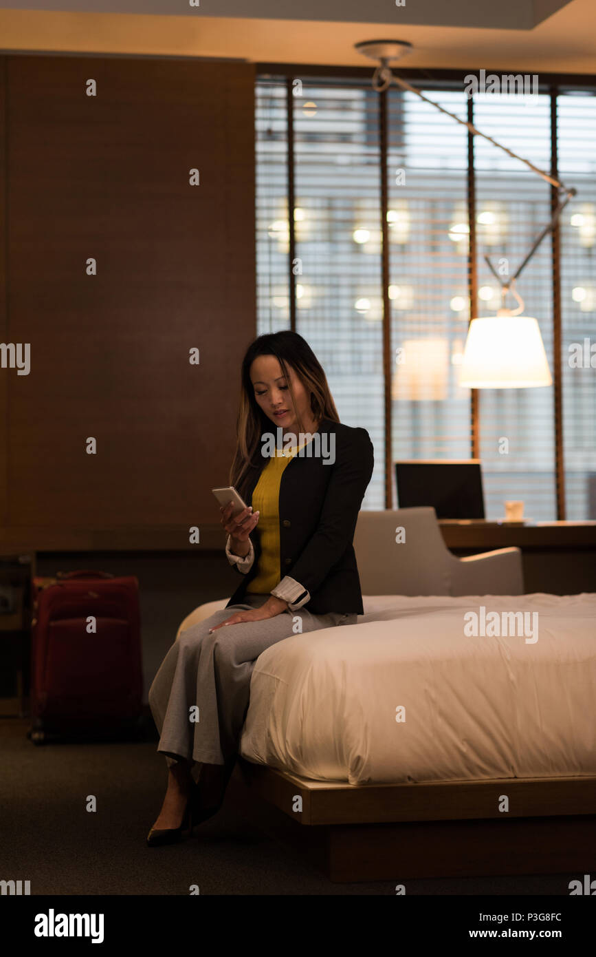 Businesswoman sitting on bed using her mobile phone Stock Photo